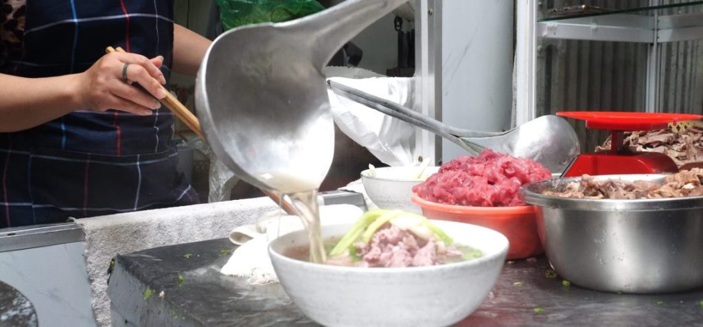 A steaming bowl of Hanoi Pho with rare beef, fresh herbs, and rice noodles